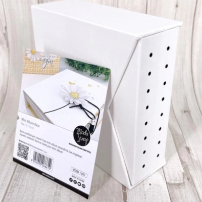 Caixa branca com orifícios e etiqueta promocional com caderno decorado.