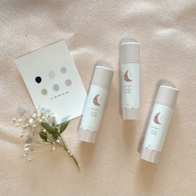 Três sticks para cuidados de pele com etiquetas de lua com ramo de flores pequenas e cartão colorido sobre tecido bege.