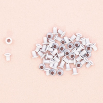 Peças pequenas brancas em forma de bucha com buraco central sobre superfície rosa clara