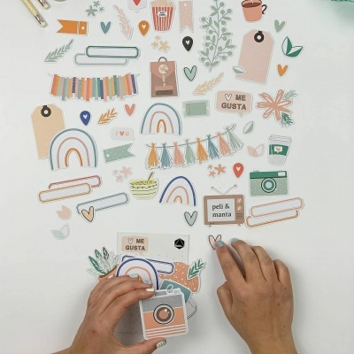 Mãos organizando recortes decorativos de papel coloridos sobre fundo branco