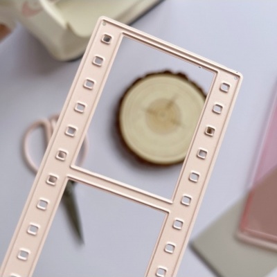 Estrutura retangular cor de rosa com pequenos orifícios, fundo branco com objeto redondo de madeira e objeto rosado translúcido