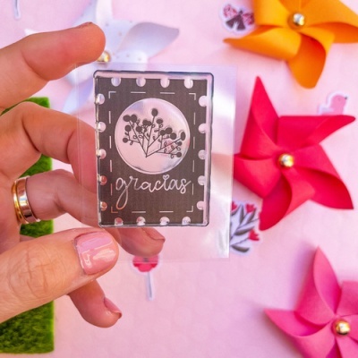 Cartão decorativo preto e branco com desenho floral e palavra 'gracias', com móbiles de papel coloridos ao fundo.