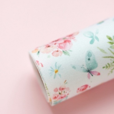 Tecido branco com padrão de flores e borboletas em cores pastel sobre superfície rosa