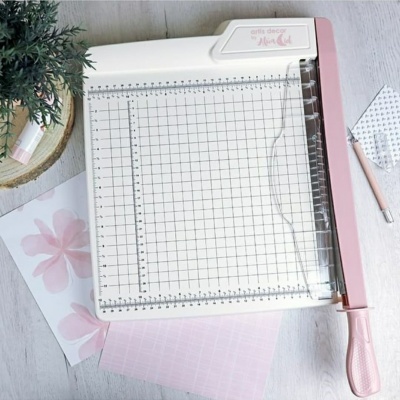 Máquina recortadora de papel branca com cabo rosa sobre mesa cinzenta com papéis e lápis