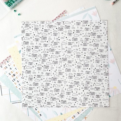 Folha de papel decorativo com padrão de câmaras fotográficas em cima de outras folhas e material de costura