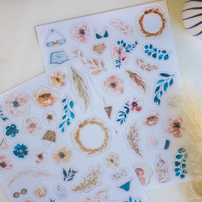 Folhas de autocolantes com ilustrações de flores, folhas e lingerie em superfície branca com plantas secas