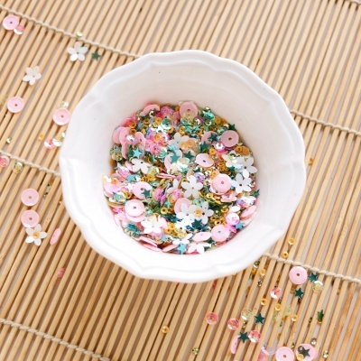 Tigela branca com lantejoulas coloridas de vários formatos sobre ripas de madeira