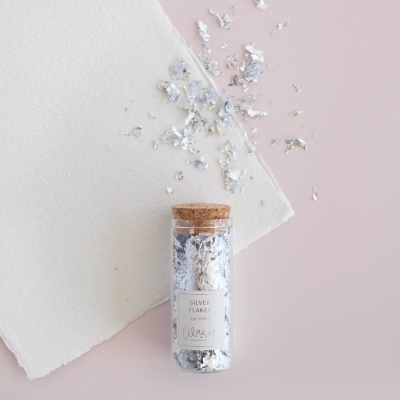 Frasco de vidro com flocos prateados e tampa de cortiça num fundo rosa com papel branco