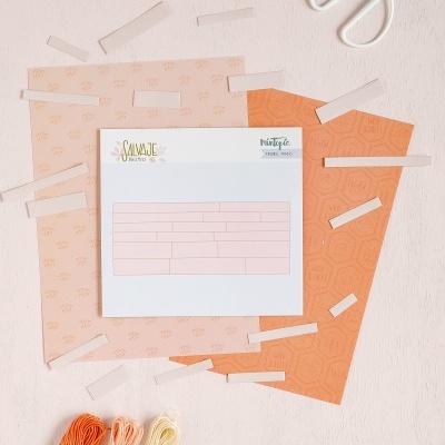 Conjunto de papéis coloridos, envelope com etiquetas SALVAJE e PRIMAVERA VERDE AMOR, tesoura branca e novelos de fio de bordado em tons de laranja, pêssego e creme.