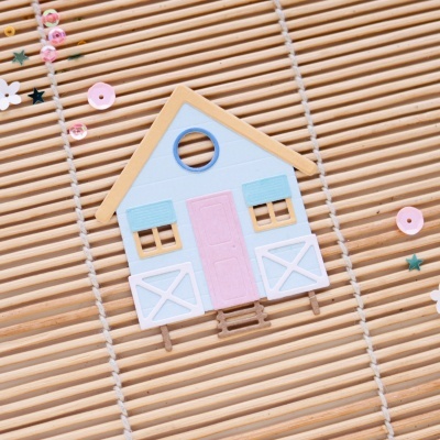 Casa decorativa em madeira com porta rosa e janelas azuis sobre superfície de bambu