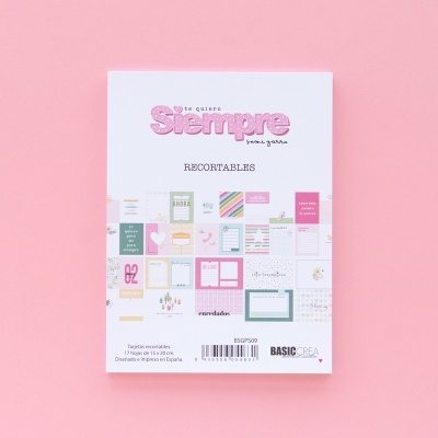 Bloco de papel para recortáveis com diversas imagens e textos coloridos em fundo branco sobre superfície rosa