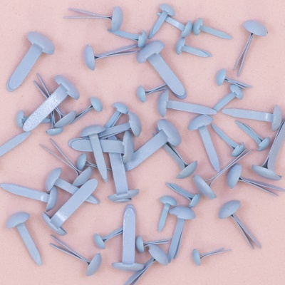 Pregos de metal prateado com cabos planos arredondados sobre fundo rosa texturado