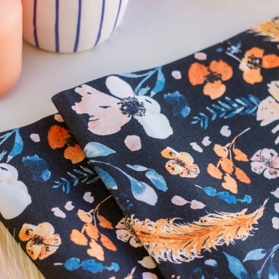 Pano floral azul com flores brancas e laranja ao lado de vela e vaso.