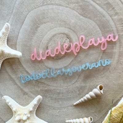 Palavras decorativas em madeira rosa e azul sobre toalha bege com estrelas-do-mar e conchas