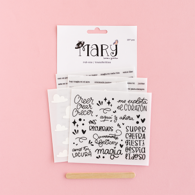 Conjunto de autocolantes com frases em espanhol em letras pretas sobre fundo branco, pau de madeira e embalagem branca sobre fundo rosa