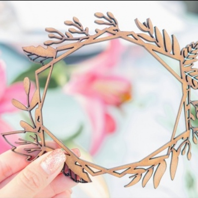 Figura decorativa em MDF com design de folhas, segurada à frente de flores cor-de-rosa desfocadas