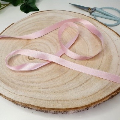 Fita de cetim rosa numa base de madeira com uma tesoura azul clara ao fundo