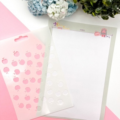 Stencil de maçãs cor-de-rosa e papel decorado com prancha de surf e chapéu sobre fundo branco e rosa.