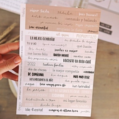 Folha decorativa com frases em espanhol de diferentes tipos de letra e cores, segurada por mão feminina.