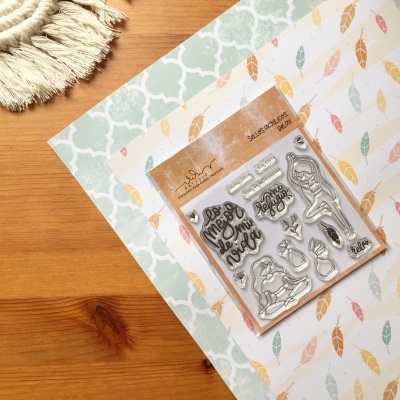 Conjunto de carimbos transparentes festivos em embalagem sobre folhas decorativas em mesa de madeira.