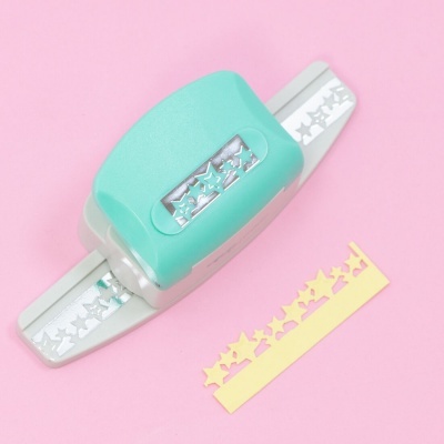 Cortador de papel verde água com padrão de estrelas e tira de papel amarelo perfurada