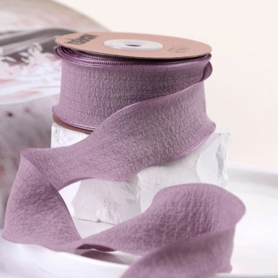 Rolo de fita lilás com textura suave sobre suporte branco.