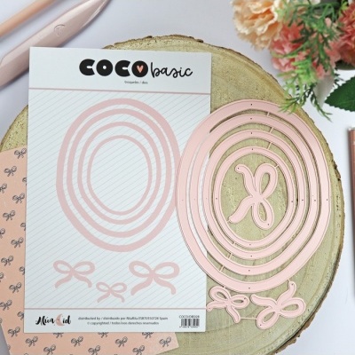 Moldes metálicos cor-de-rosa em formato oval com detalhes de laços sobre cartão e superfície de madeira