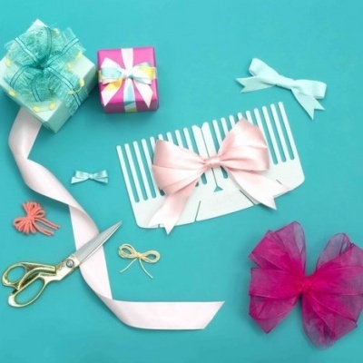Laços de fita coloridos, pente, tesoura e caixas de presente sobre fundo azul.