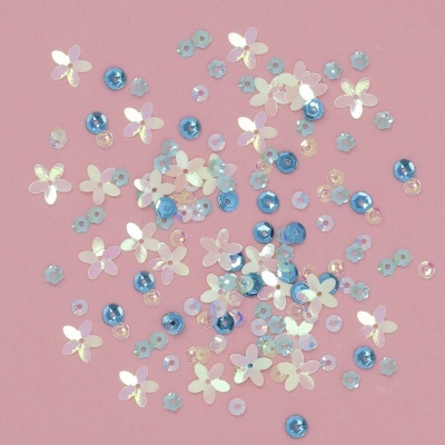 Lantejoulas florais e redondas azuis, lilás e brancas num fundo rosa