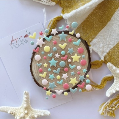 Peças decorativas coloridas sobre madeira com cartão, toalha e estrelas-do-mar ao redor.