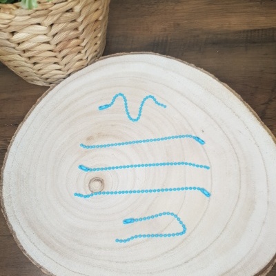 Colar azul em contas sobre tronco de madeira circular com planta em vaso de palha