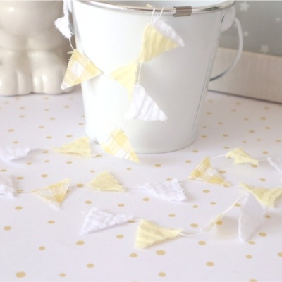 Guirlanda de tecido com triângulos brancos e amarelos sobre superfície branca com pontos dourados