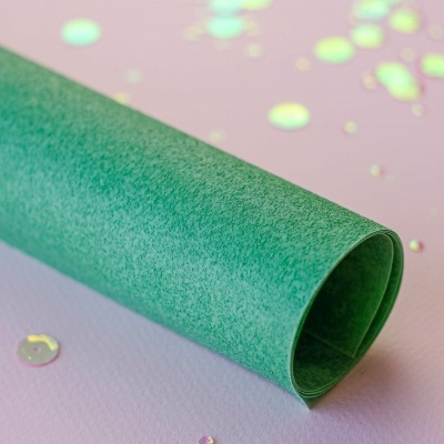 Rolo de papel verde texturado e confetes brilhantes sobre fundo rosa