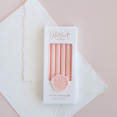 Conjunto de 6 varetas de cera cor-de-rosa em caixa branca com selo floral sobre papel branco e fundo rosa claro