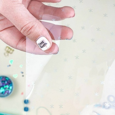 Mão segurando película transparente decorada com flocos de neve brancos.