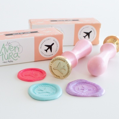 Carimbos de cera rosa com selos coloridos e caixas de embalagem à cor bege e branca com avião preto