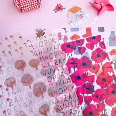 Papéis decorativos coloridos com padrões de letras, árvores, flores e objetos sobre fundo rosa matelassado.