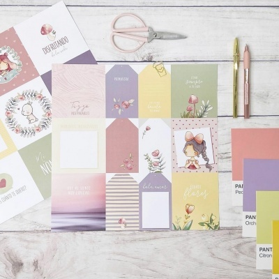 Etiquetas coloridas, tesouras, canetas e amostras Pantone sobre uma mesa de madeira clara