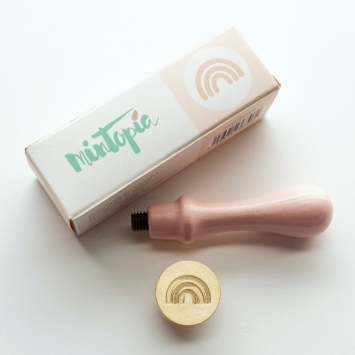 Selo de madeira com punho rosa e caixa branca com nome Mintopia e arco-íris