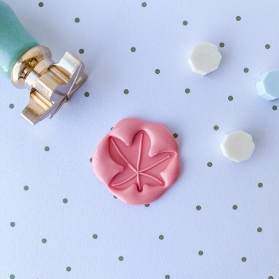 Selo de lacre com cabo verde ao lado de lacre rosa com desenho de folha e lacres brancos e azul claro