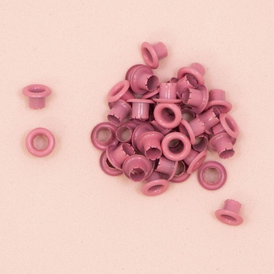 Ilhós rosa em metal com acabamento brilhante sobre fundo cor de rosa