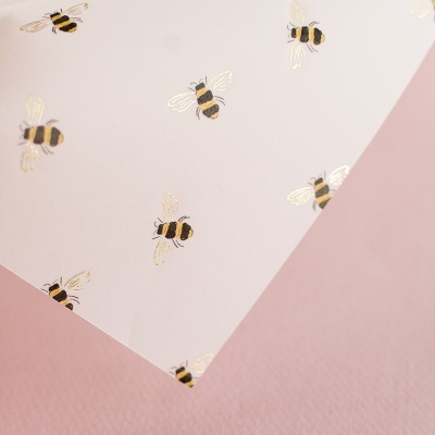 Papel branco com padrão de abelhas douradas e pretas sobre superfície rosa