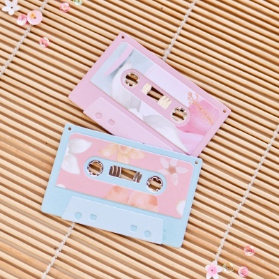 Duas cassetes coloridas rosa e azul com desenhos florais sobre superfície de bambu