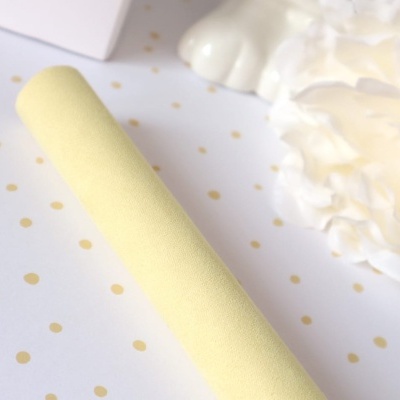 Rolo amarelo claro sobre superfície branca com pontos dourados, ao lado de flor branca