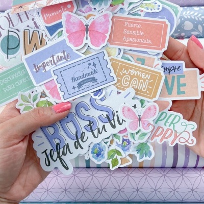 Mãos segurando autocolantes coloridos sobre tecidos em tons pastel com padrões variados