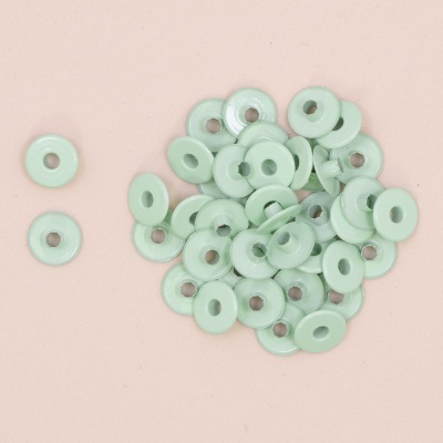 Pequenas arruelas planas verde claro com orifício central sobre fundo rosa claro