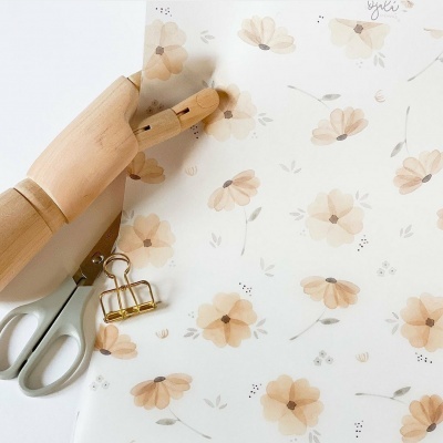 Folha de papel floral bege com mão de madeira, tesoura cinza e clipe dourado