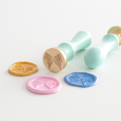 Dois selos de lacre com cabo azul claro estampados com laço e selos de cera coloridos com o mesmo padrão