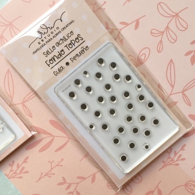 Selo acrílico com padrão de pontos pretos em embalagem de plástico transparente sobre fundo rosa com padrão floral.