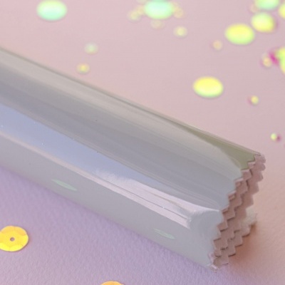 Objeto branco brilhante com corte em ziguezague sobre superfície rosa com lantejoulas